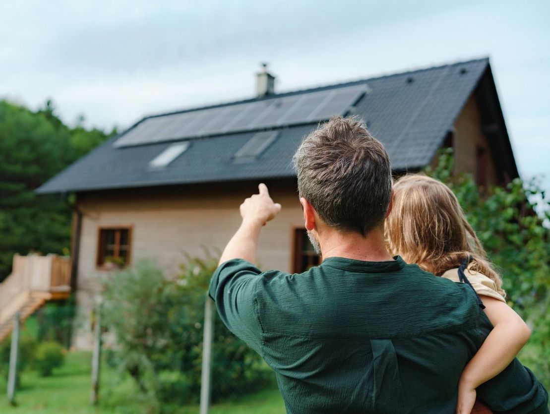 padre sosteniendo a niña y señalando a placas solares del techo de su casa
